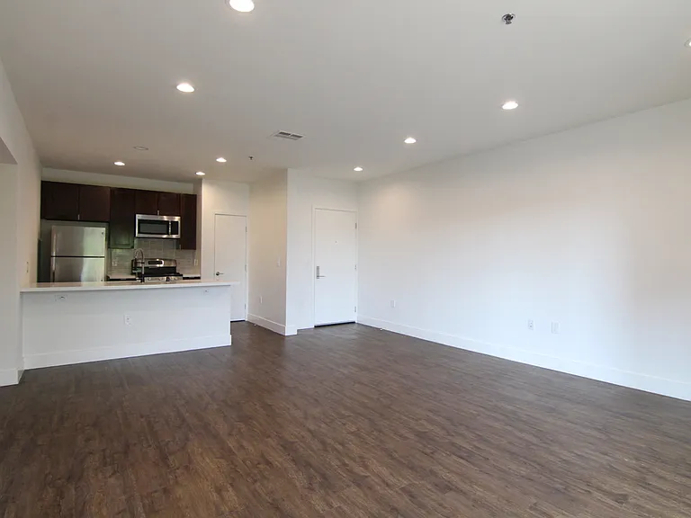 Hardwood floored living room with can lights and view of kitchen.