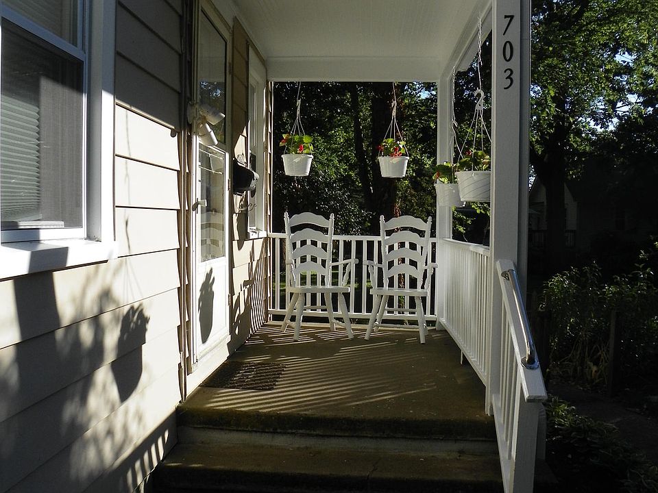 Front porch at the end of the sidewalk includes planters and 2 wooden chairs.