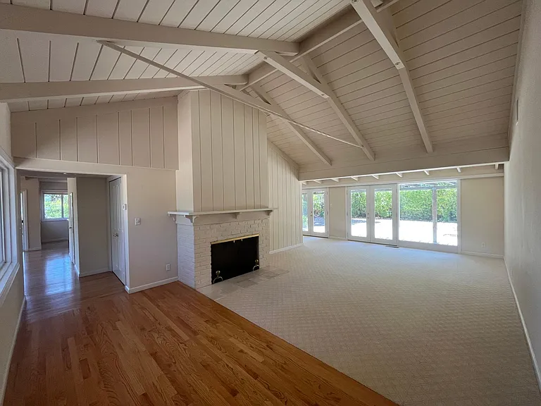 Bright, airy living room features high vaulted ceiling, two wood burning fireplaces, plush carpeting and floor-to-ceiling glass panels and patio doors that flows to a relaxing backyard with a trellis patio cover surrounded by mature trees.