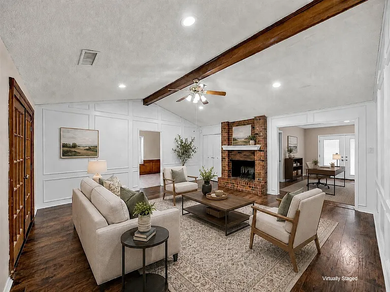 Living area featuring a brick fireplace, vaulted ceiling with wood beam, and rich wood-finish flooring