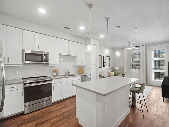 Finish Package II kitchen with stainless steel appliances, white cabinetry, white tile backsplash, grey quartz countertops, and hard surface flooring