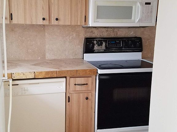 Galley kitchen has fridge, flat top stove, dishwasher, microwave, travertine tile countertops