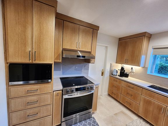 Kitchen features a spacious pantry with pull-out drawers, LG microwave, LG 4-burner induction cooktop, large multi-function oven, and a lighted hood with multi-level exhaust. Durable stone flooring completes this modern, functional space.