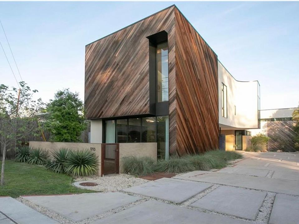 Street view of townhouse, including grassy private courtyard in front and large glass wall that fully opens.