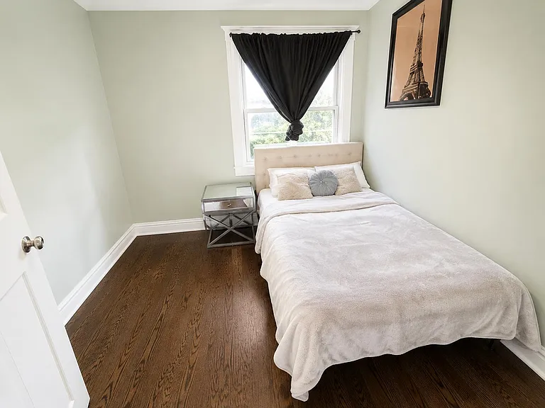 Private bedroom with a full bed, nightstand, and hardwood floors, plus a large window for natural light.