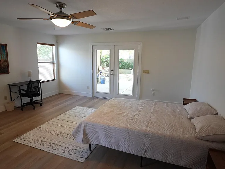 Spacious bedroom with wood-look floors, ceiling fan, and patio access through French doors plus a dedicated desk nook.