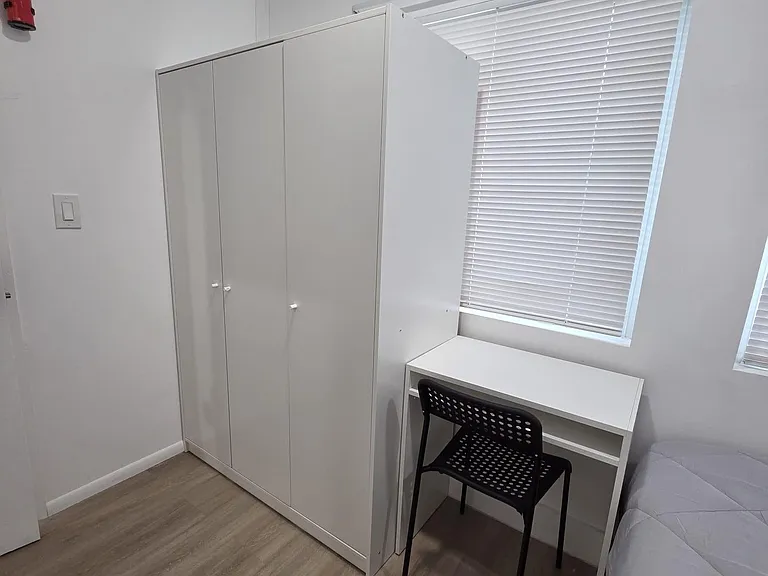 Furnished bedroom with a wardrobe, dedicated desk space, and window blinds for adjustable light and privacy.