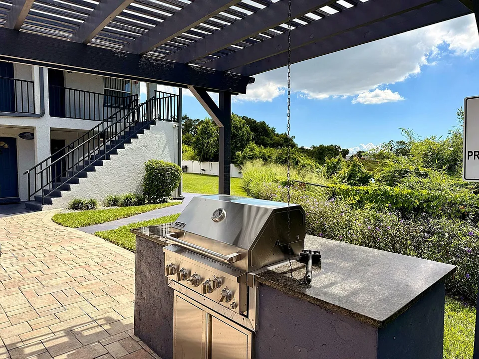 Charming outdoor area featuring a sleek stainless steel grill under a stylish pergola, surrounded by lush greenery and a cozy patio setting.