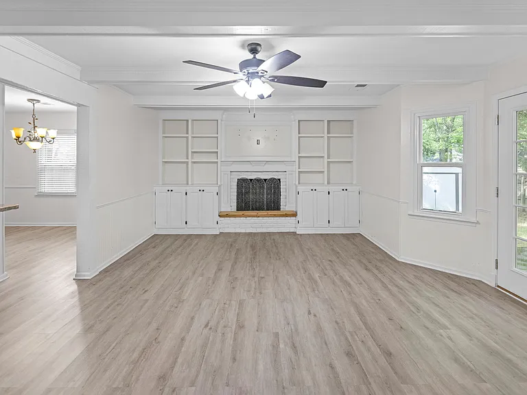 Spacious living room showcasing full-wall built-ins, a classic fireplace, and lush garden views through large windows.