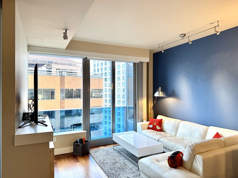 Bright living area with floor-to-ceiling windows, hardwood floors, and downtown views