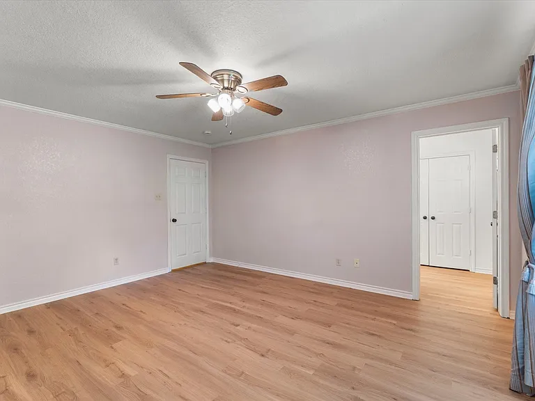 Spacious room with wood-finish flooring, ceiling fan with integrated lighting, and white trim molding