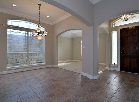 The formal dining area has tile flooring, crown molding, an exterior atrium just outside the windows and has an arched opening separating it from the living area.