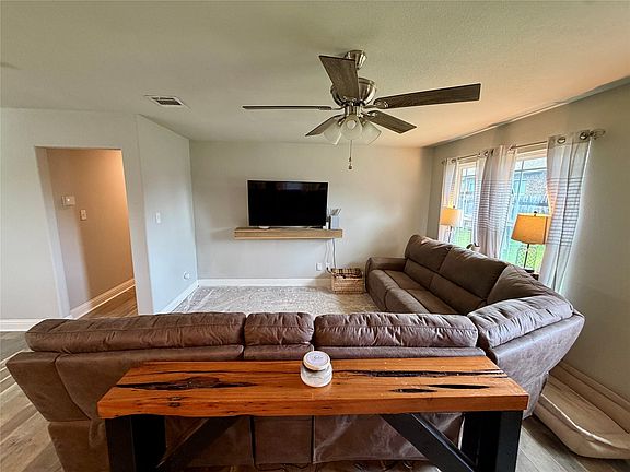 Living area featuring light gray wall paint, wood-finish flooring, and a ceiling fan with integrated lighting