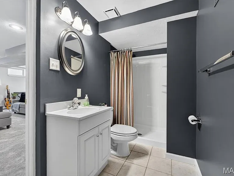 Bathroom featuring a white vanity with integrated sink, chrome faucet, oval mirror, and three-light vanity fixture