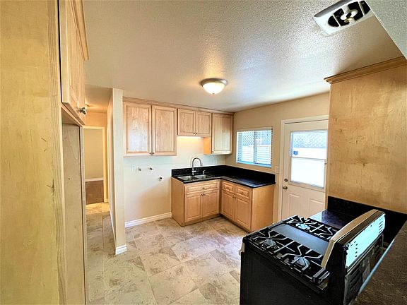 Kitchen with tile flooring, maple cabinets, granite counters and new stainless range and washer hookups. Hall leads to bedrooms and bathroom.