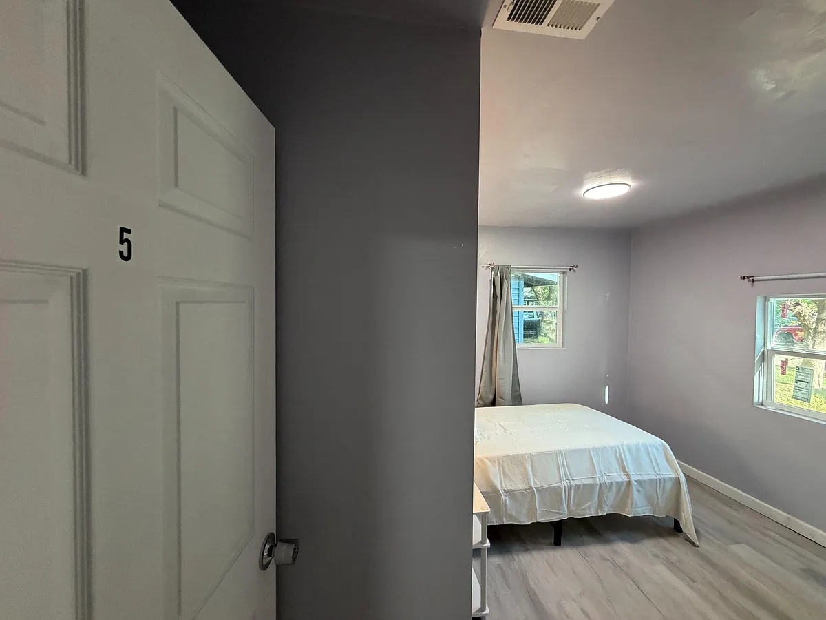 Photo 2 of 7 - Huntington Dr - Arlington, TX Private bedroom with a bed setup, ceiling light, and two windows for natural light and outdoor views. - Huntington Dr