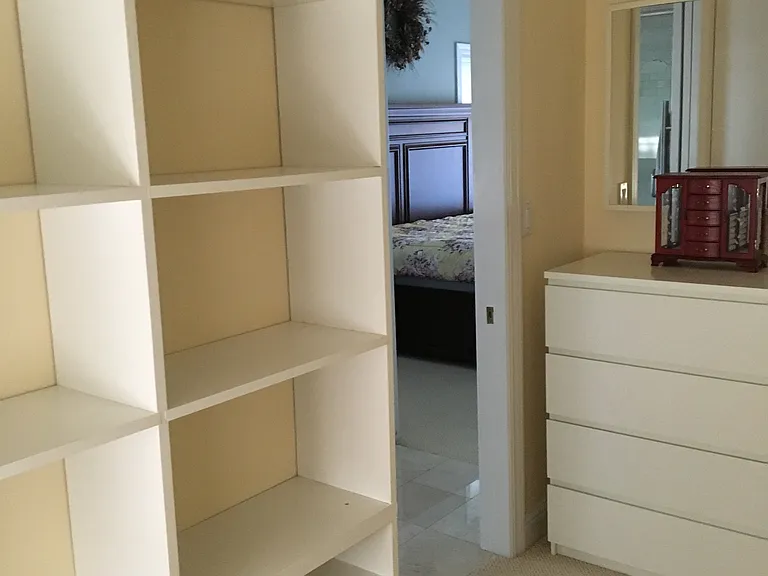 Primary bedroom walk in closet with white cabinets and attached mirror.