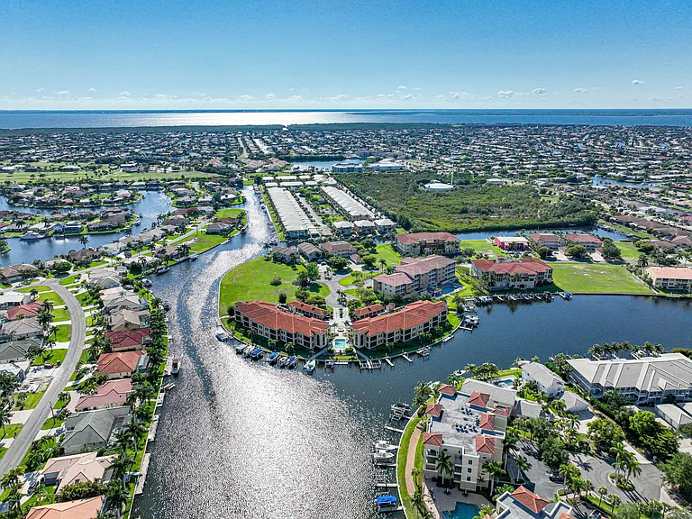 Aerial from east looking west toward Charlotte Harbor beyond. Condo complex is surrounded by water. See sunrises right from the unit. Sunsets, about a one minute walk to the west. Your Florida Paradise awaits.