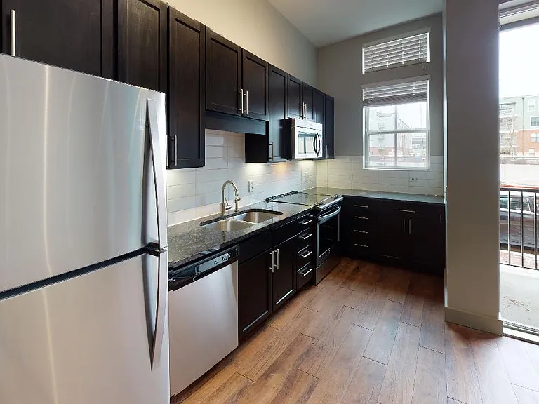 Apartment kitchen with stainless steel appliances, granite countertops and wood-style flooring.