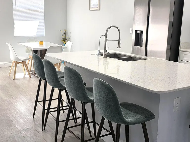 Open kitchen with a large quartz island, bar seating, and stainless-steel refrigerator, plus a nearby dining area.