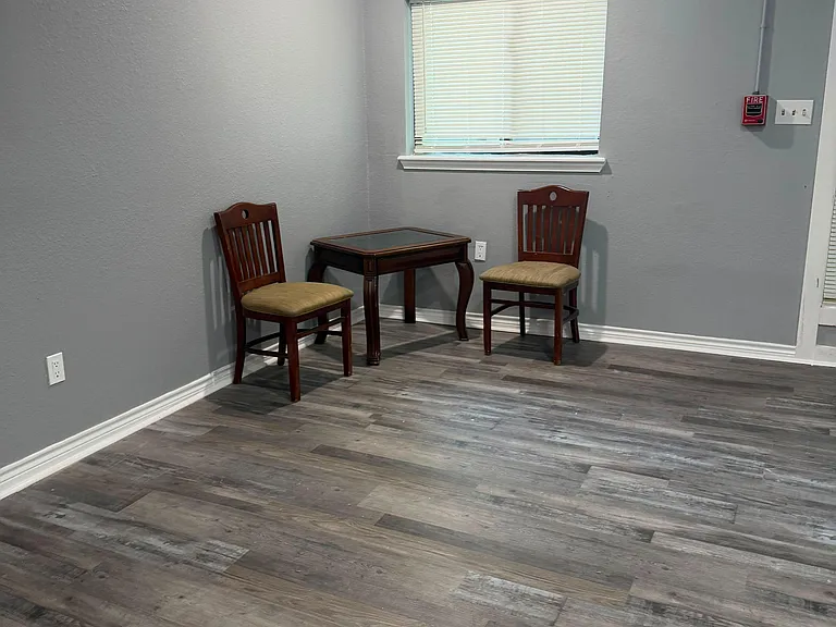 Open common area with durable plank flooring and a window with blinds, offering space for a small table or reading nook.