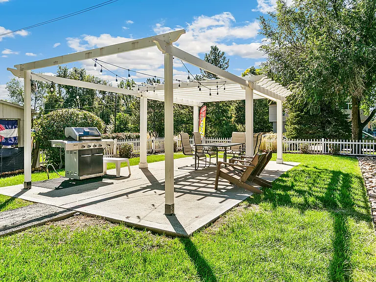 Charming backyard area featuring a pergola with string lights, a modern grill, and comfortable seating, perfect for outdoor entertaining.