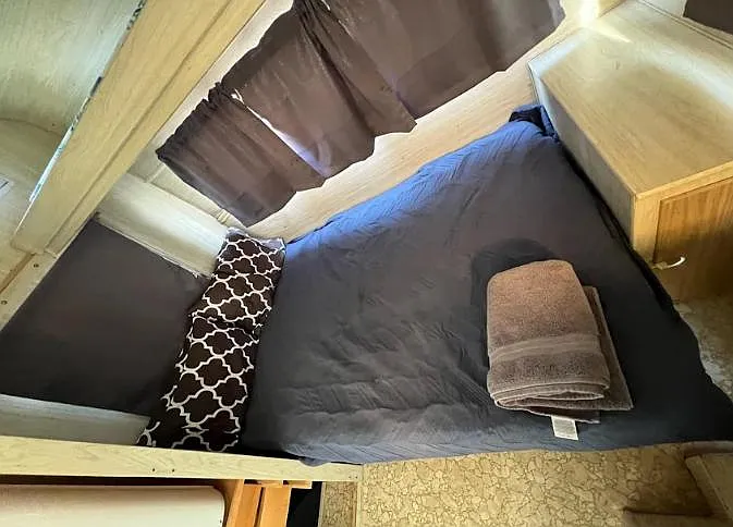 Compact sleeping nook with a twin bed, side table, and window coverings for added privacy and light control.