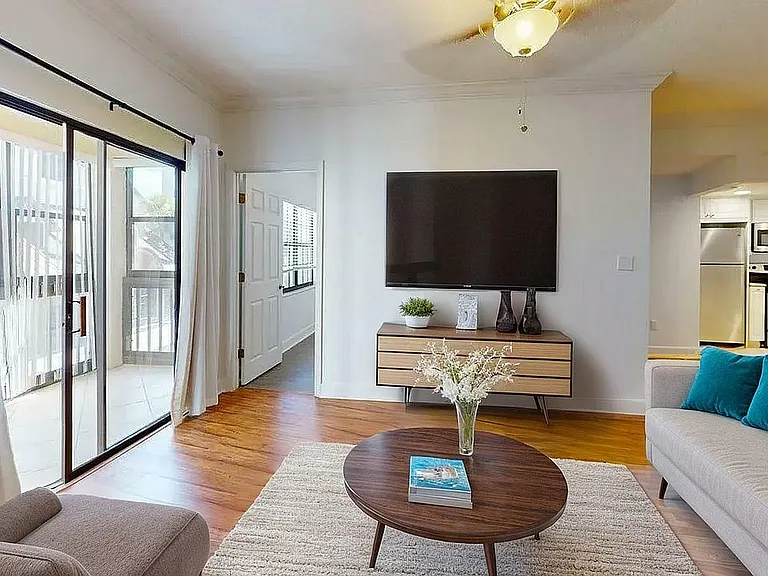 Bright and modern living room with large sliding glass doors, cozy seating area, and stylish open kitchen in a contemporary apartment.