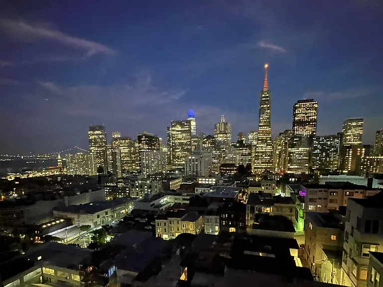 Photo from 267-273 Green Street shows a breathtaking nighttime view of San Francisco's skyline, featuring the glowing Transamerica Pyramid and the distant Bay Bridge under a deep blue sky.