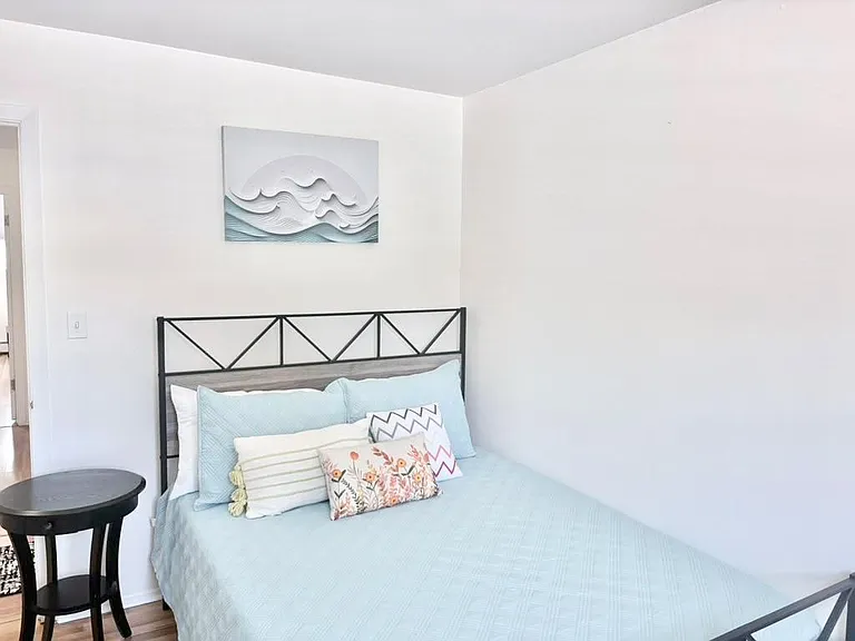 Furnished bedroom with a full bed, side table, and clean wall space for added storage or a desk setup.