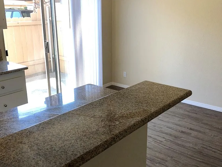 View of kitchen serving bar and dining area with sliding glass door to private porch at Plaza Verde Apartments in Escondido, California.
