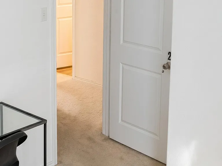 Carpeted interior area with a hallway entry and access to an adjacent room, featuring clean walls and a simple layout.