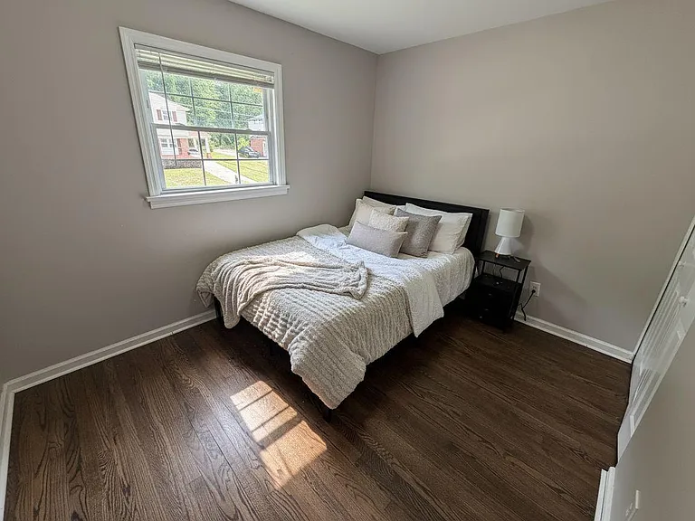 Private bedroom with hardwood floors, a large window for natural light, and space for a nightstand and storage.