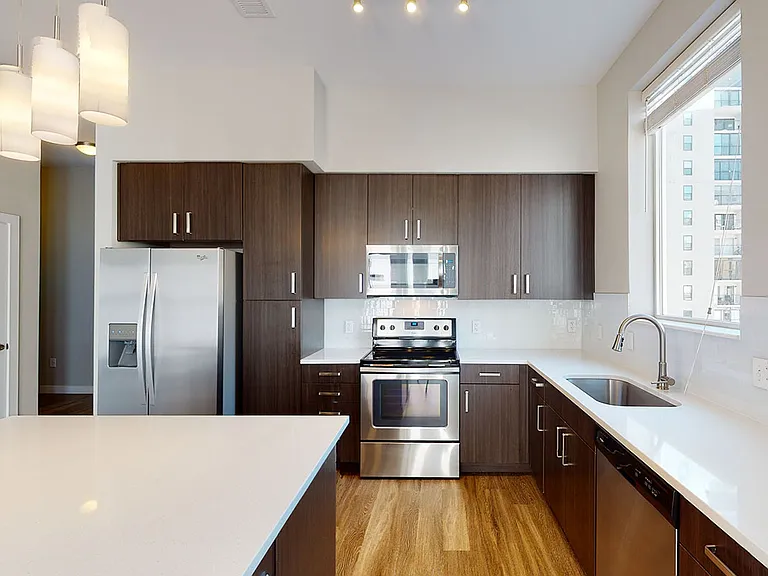 Apartment kitchen with stainless steel appliances, quartz countertops and wood-style flooring.
