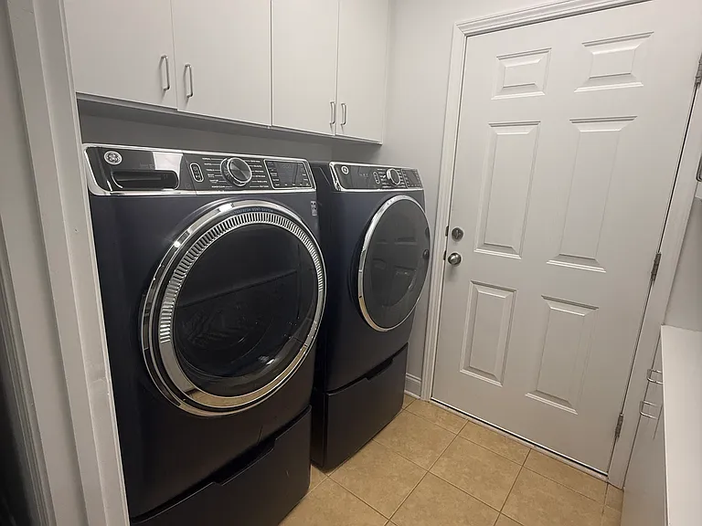 Spacious laundry room with modern front-load washer and dryer, extensive built-in cabinets, and a folding counter.