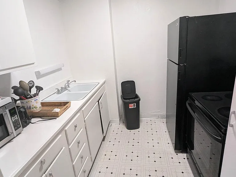 Compact galley kitchen with ample cabinetry, double-basin sink, microwave, and full-size range and refrigerator.