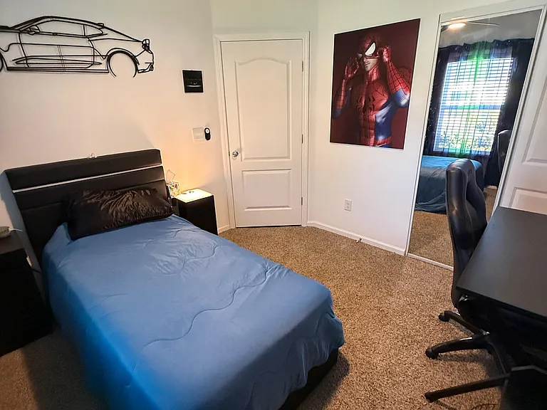 Furnished bedroom with a ceiling fan, mirrored closet doors, and space for a desk, plus a window with blinds for privacy.