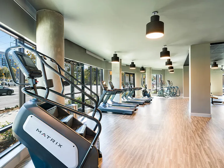 A light-filled fitness area with cardio equipment, expansive windows, and an open layout that supports movement, focus, and everyday wellness.
