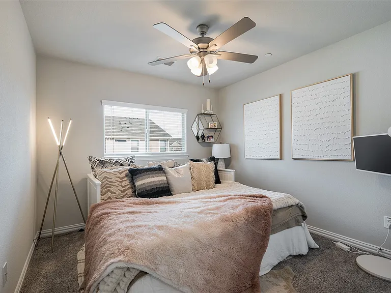 Carpeted room featuring a ceiling fan with light fixture, built-in shelving, window with blinds and drapery, and a decorative area rug