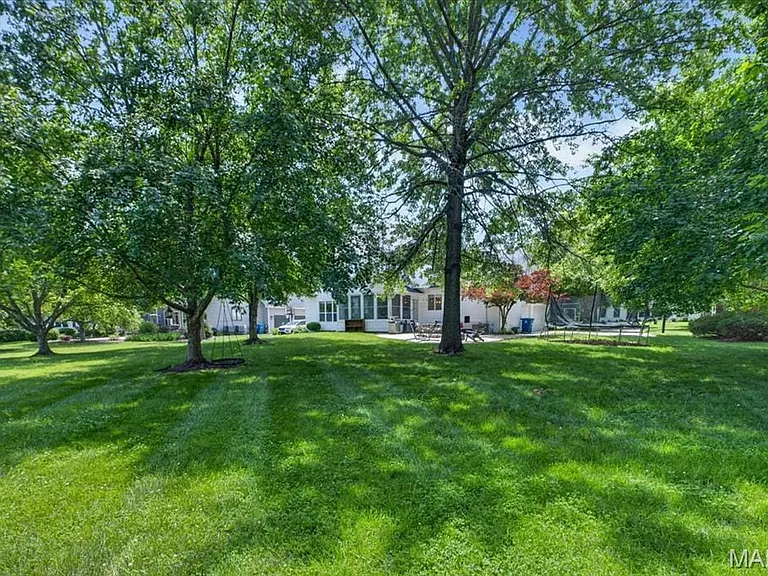 Expansive rear yard featuring mature trees, a lush lawn, and a light-toned exterior with multiple windows