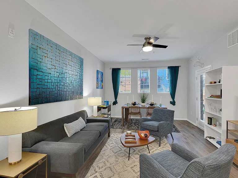 Inviting modern living room with stylish gray furniture, vibrant art pieces, and abundant natural light from large windows.