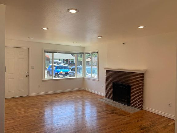 Spacious living room with natural light, hardwood floors, recessed LED lights, fireplace.