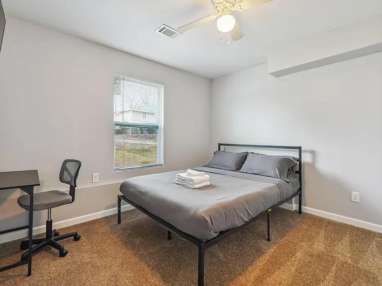 Furnished bedroom with a full bed, work desk, and a window with blinds for comfortable daily living.