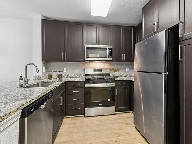 Renovated Package I kitchen with espresso cabinetry, speckled granite countertops, beige subway tile backsplash, stainless steel appliances, and hard surface flooring