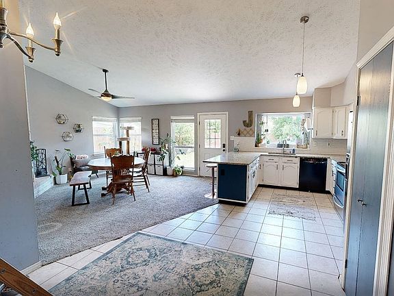 Open-concept living space featuring a kitchen with white cabinetry and a blue island, tile flooring, and pendant lighting