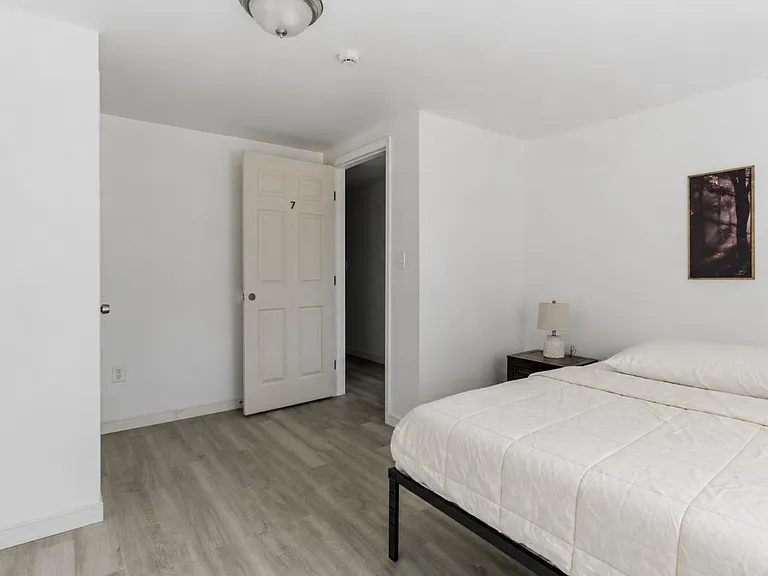 Spacious bedroom with wood-look flooring, a comfortable bed setup, and convenient nightstand lighting for everyday use.