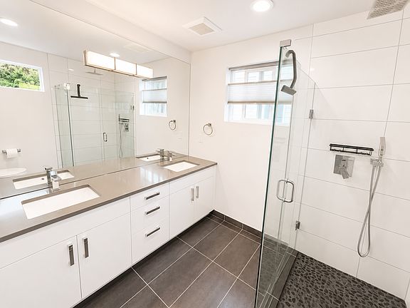 Primary bathroom has a double vanity, great natural light, rainfall shower head, and newly-tiled river rock shower floor.