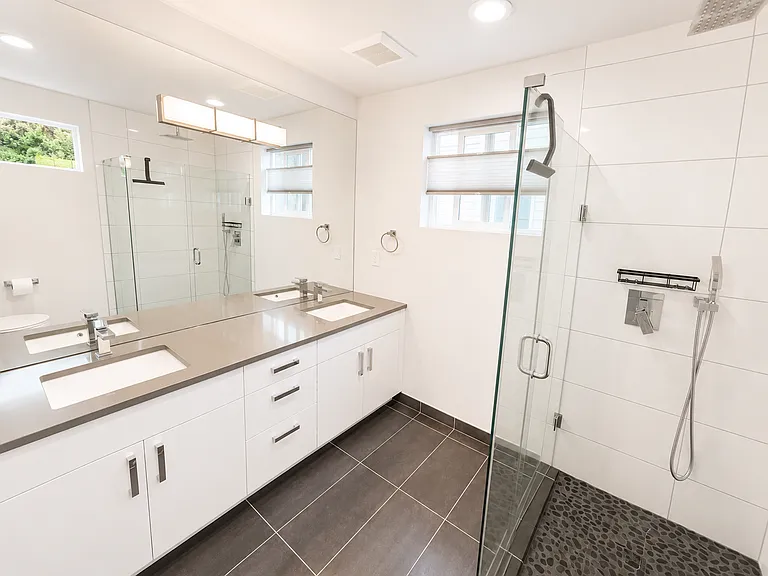 Primary bathroom has a double vanity, great natural light, rainfall shower head, and newly-tiled river rock shower floor.