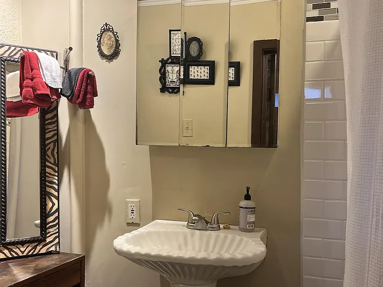 Compact bathroom with pedestal sink, mirrored medicine cabinet, and tub/shower with tile surround and curtain.