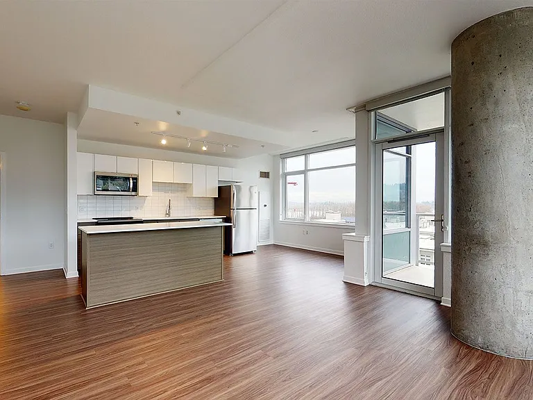 Apartment kitchen with stainless steel appliances, dining and living room with wood-style flooring.